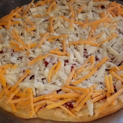 A close up of garlic herb pizza dough topped with sauce, mozzarella, and a sprinkle of cheddar.