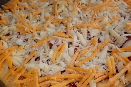 A close up of garlic herb pizza dough topped with sauce, mozzarella, and a sprinkle of cheddar.