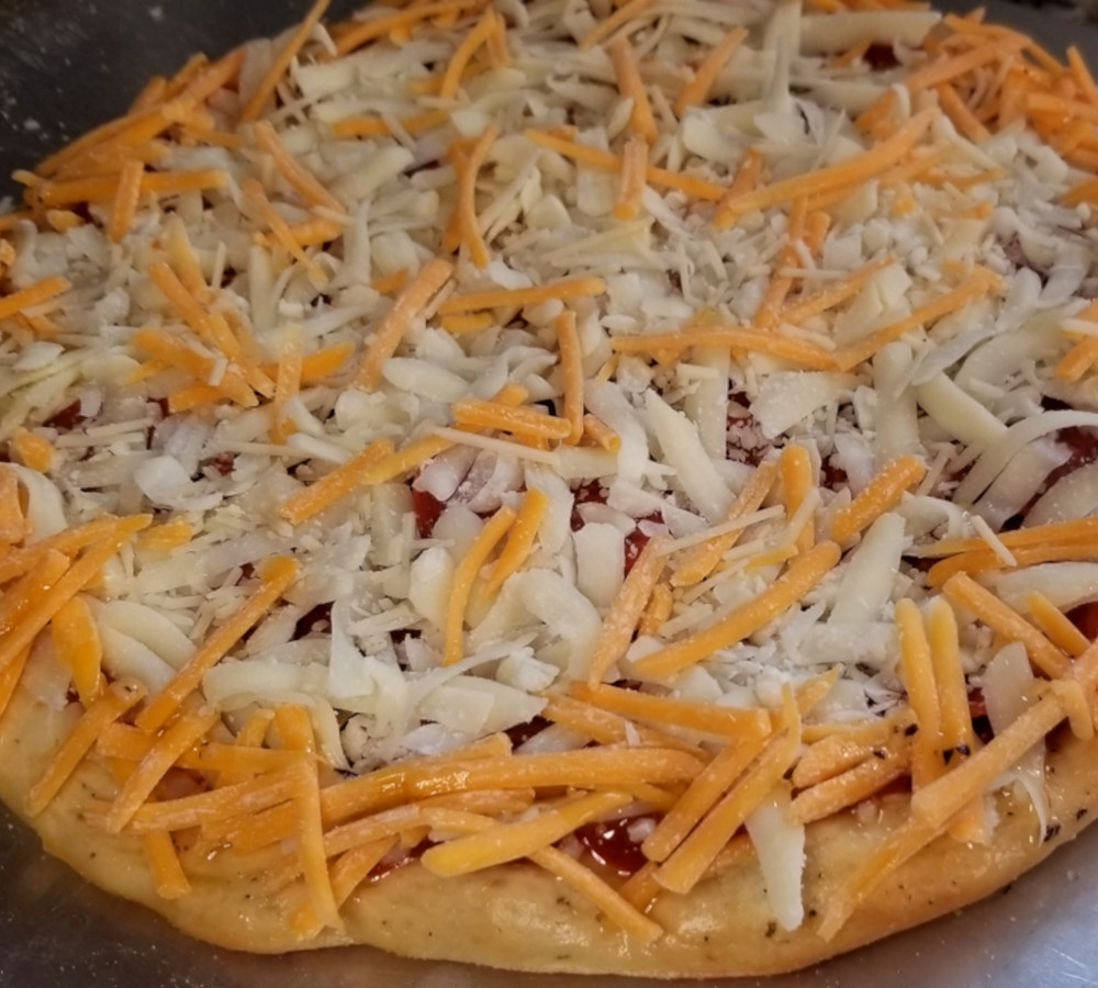 A close up of garlic herb pizza dough topped with sauce, mozzarella, and a sprinkle of cheddar.