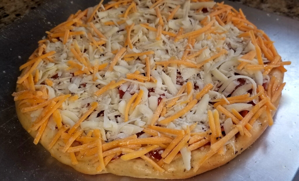 A close up of garlic herb pizza dough topped with sauce, mozzarella, and a sprinkle of cheddar.