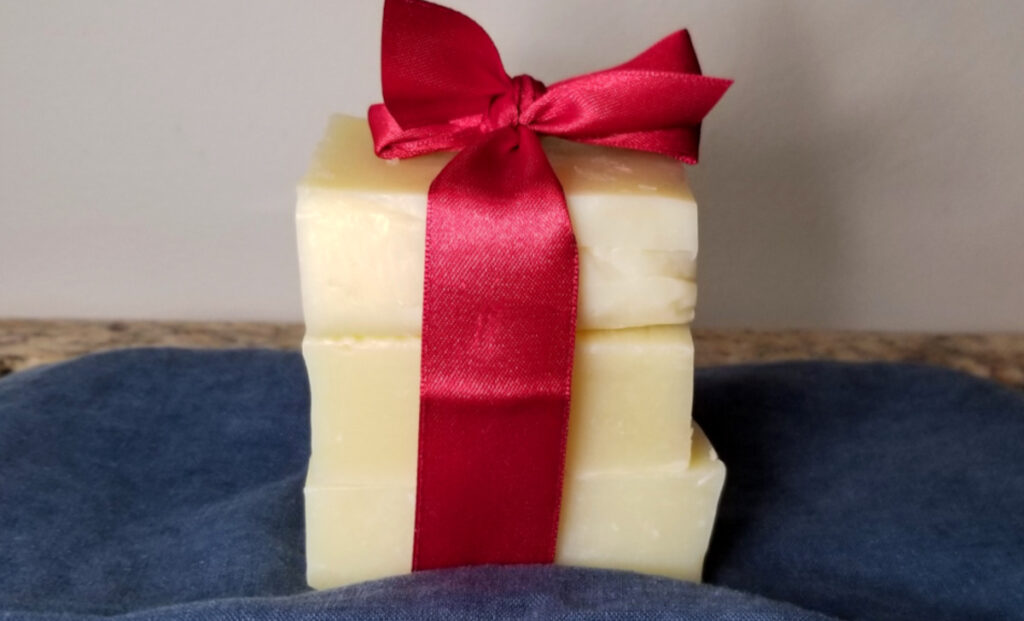 Homemade soap wrapped in a red bow and stacked atop a blue cloth.