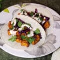 air fryer sweet potato tacos with cilantro, cabbage, and creamy sriracha on a flower patterned plate.