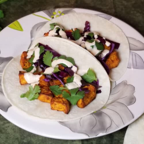 air fryer sweet potato tacos with cilantro, cabbage, and creamy sriracha on a flower patterned plate.