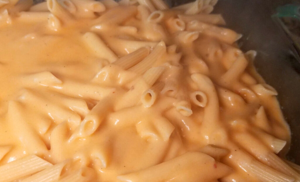 A close up of penne in a baking dish with cheese sauce poured over the top. 