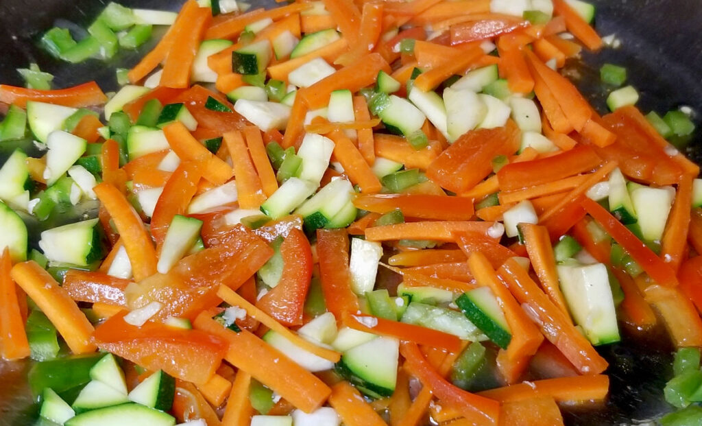 Zucchini, carrots, and red bell pepper cooking in a pan.