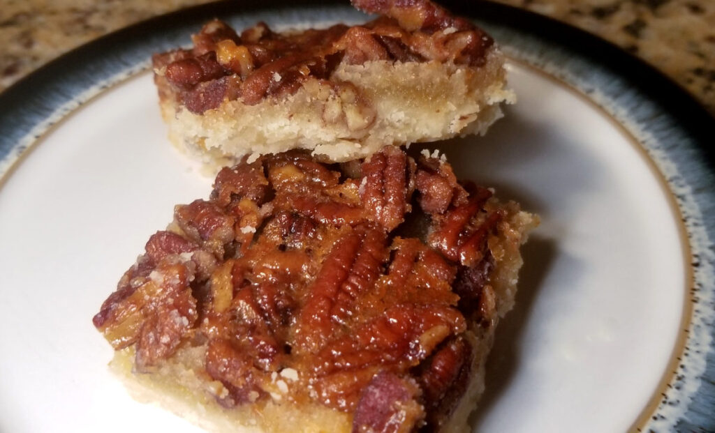 pecan bars with shortbread crust stacked on a plate with a blue rim. 