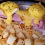 A close up of eggs benedict with crispy home fries.