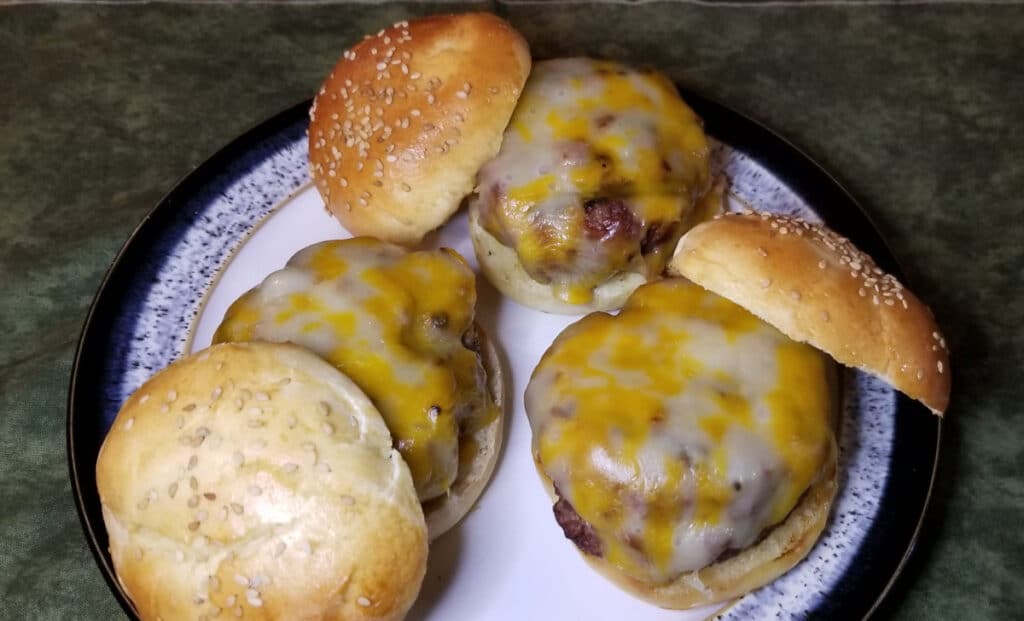 Three cheese burgers on a plate with the top homemade buns leaning against them.