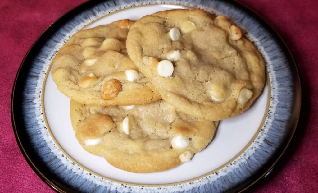 Three macadamia nut white chocolate cookies stacked on a plate. 