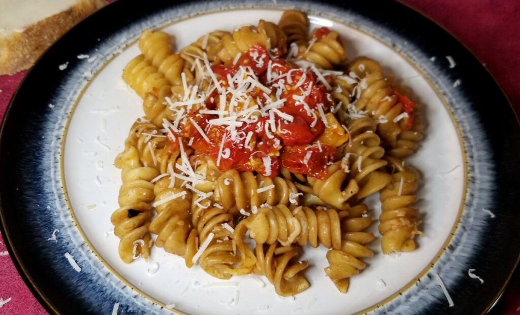 Pasta with burst cherry tomato sauce on a plate, sprinkled with parmesan and buttered bread. 