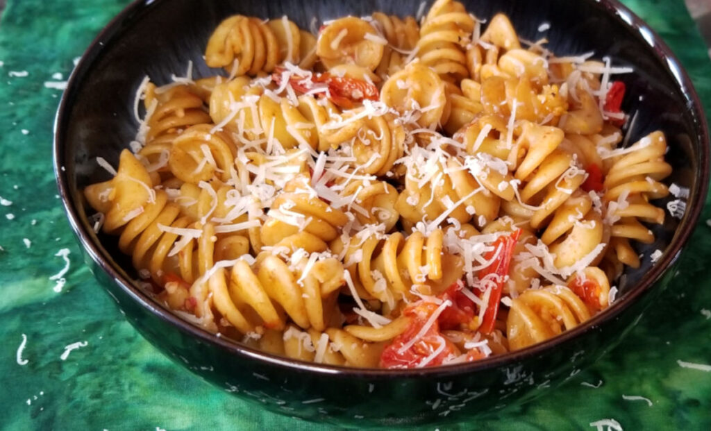 tomato pasta with shredded parmesan in a bowl on a green background.