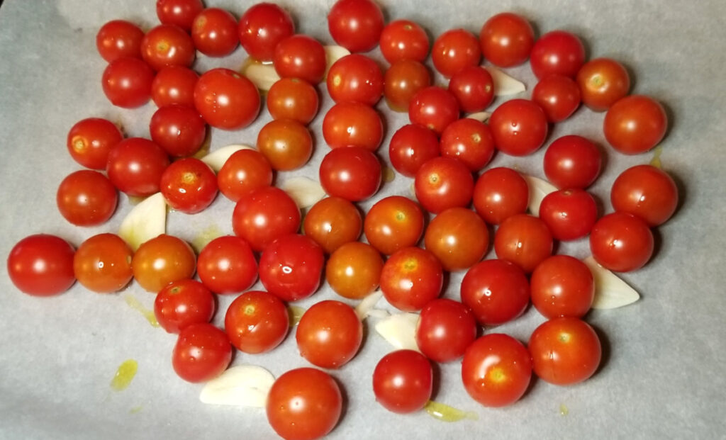 Cherry tomatoes and sliced garlic drizzled with olive oil on a parchment lined cookie sheet.
