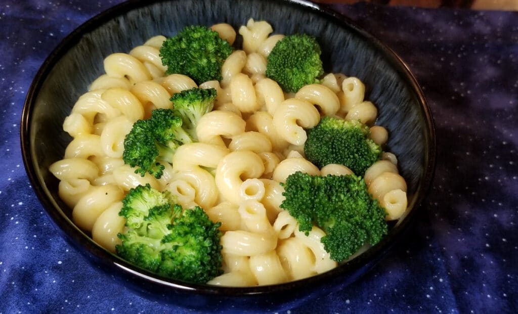 Cavatappi and cheese with broccoli in a bowl on a blue background. 
