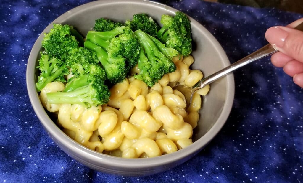 A bowl of pressure cooker macaroni and cheese with broccoli. A fork is placed in the bowl, ready to grab a bite. 