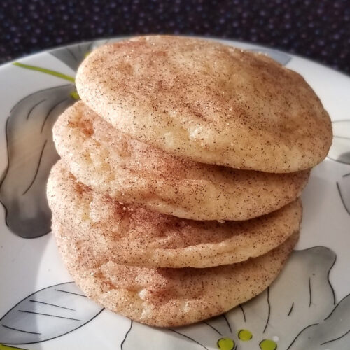 Snickerdoodles stacked on a floral plate.