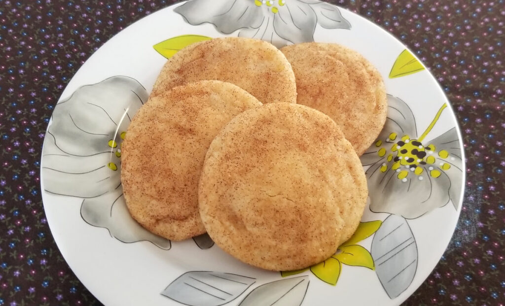 Four snickerdoodles overlapping on a floral plate. 