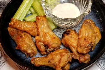 A close up of air fryer wings with ranch and celery.