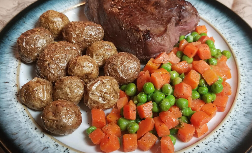 Crispy baby potatoes on a plate with carrots, peas, and steak.