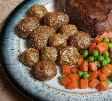 Air fryer potatoes on a plate with peas,, carrots, and steak