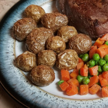 Air fryer potatoes on a plate with peas,, carrots, and steak