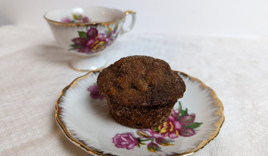 A cinnamon sugar coated banana muffin on a floral plate, with a matching tea cup in the background.