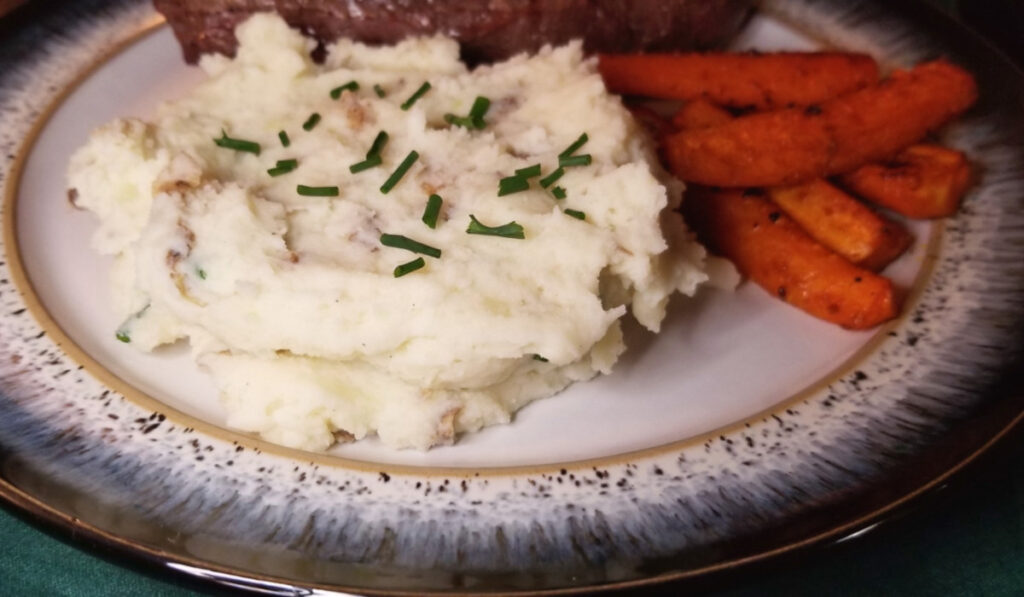 Mashed potatoes sprinkled with chives alongside roasted carrots.