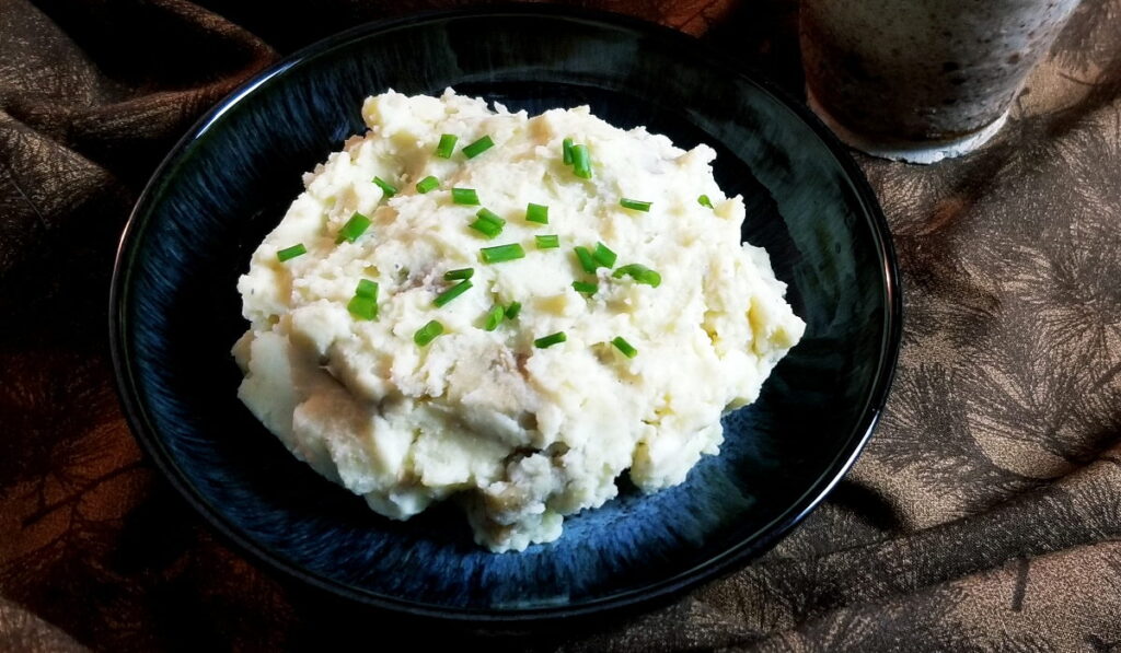 Sour cream mashed potatoes with herbs sprinkled over them, in a blue bowl with a brown background.