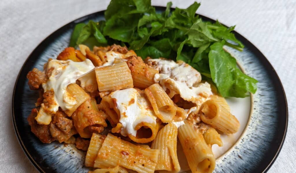 Baked italian sausage rigatoni on a plate with a small arugula salad.