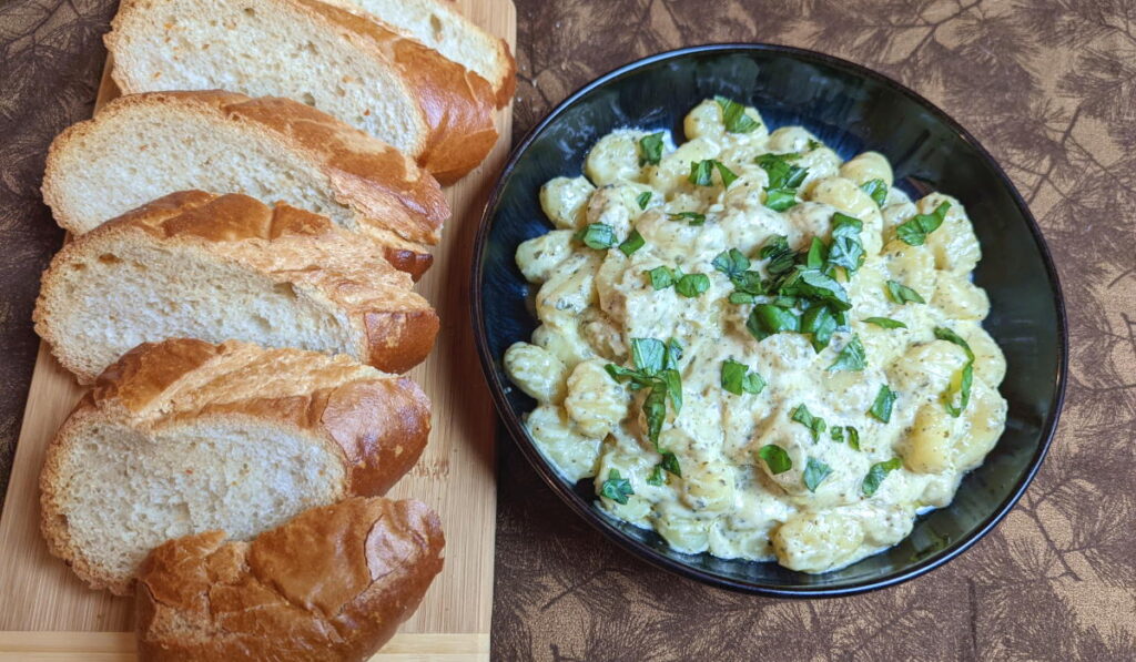 Pesto cream gnocchi in a bowl alongside cut French bread. 