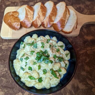 gnocchi coated in a creamy pesto sauce, served alongside some sliced French bread.