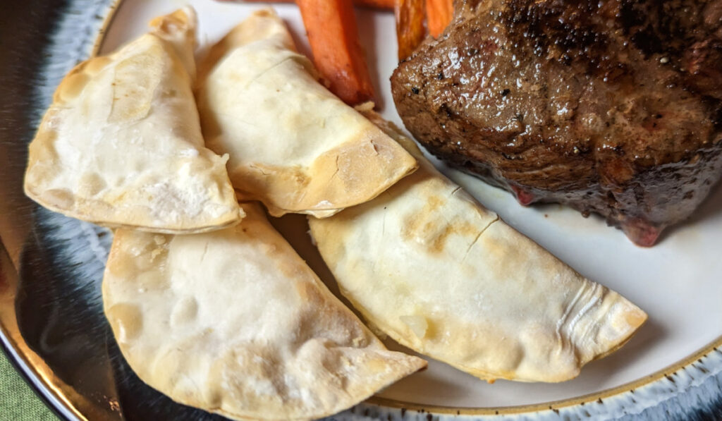 Perogies served with carrots and steak.