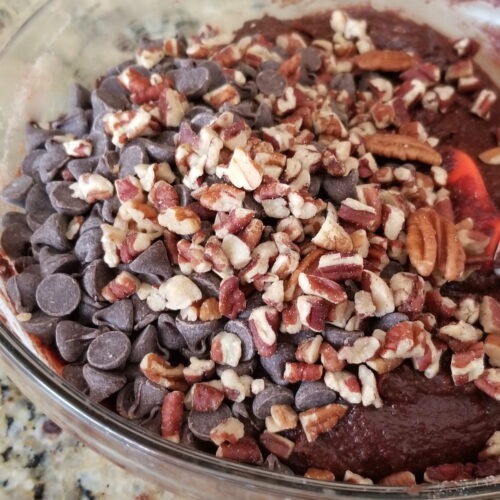 Pecans and chocolate chips scattered on top of brownie batter in a bowl.