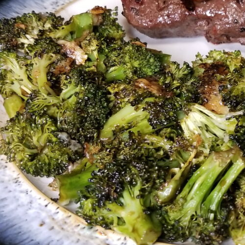 A close up of balsamic broccoli with steak and mushrooms in the background.