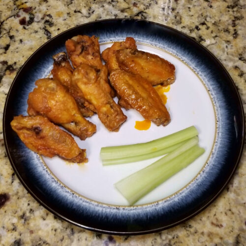 Air fryer wings coated in buffalo wing sauce, served with celery.