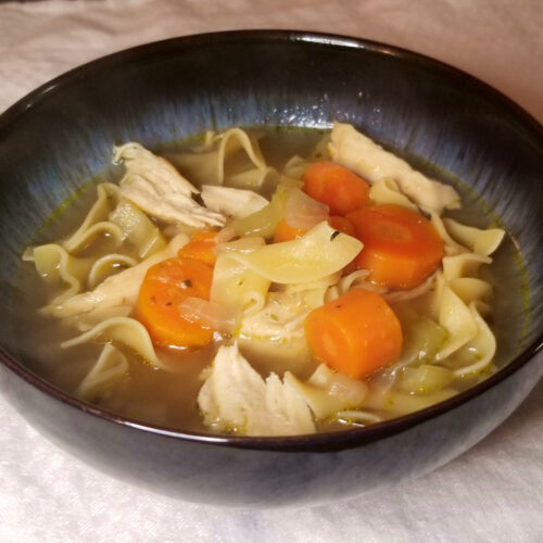 Chicken noodle soup in a blue bowl.