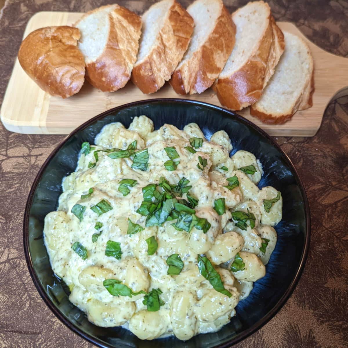 gnocchi coated in a creamy pesto sauce, served alongside some sliced French bread.