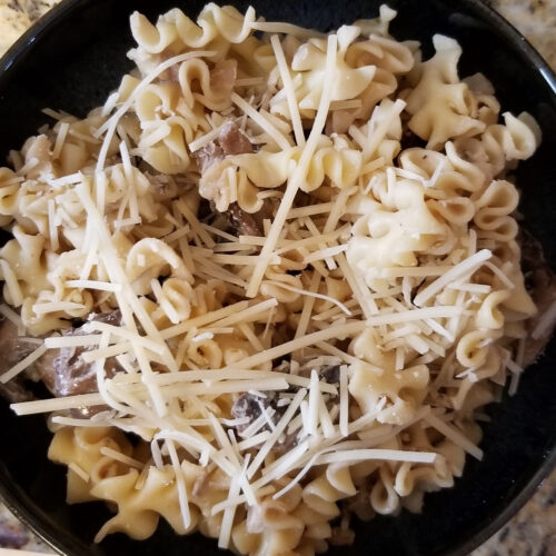 A close up of a bowl of balsamic mushroom pasta topped with shredded parmesan.