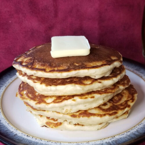 Stacked pancakes on a plate, topped with a pat of butter.