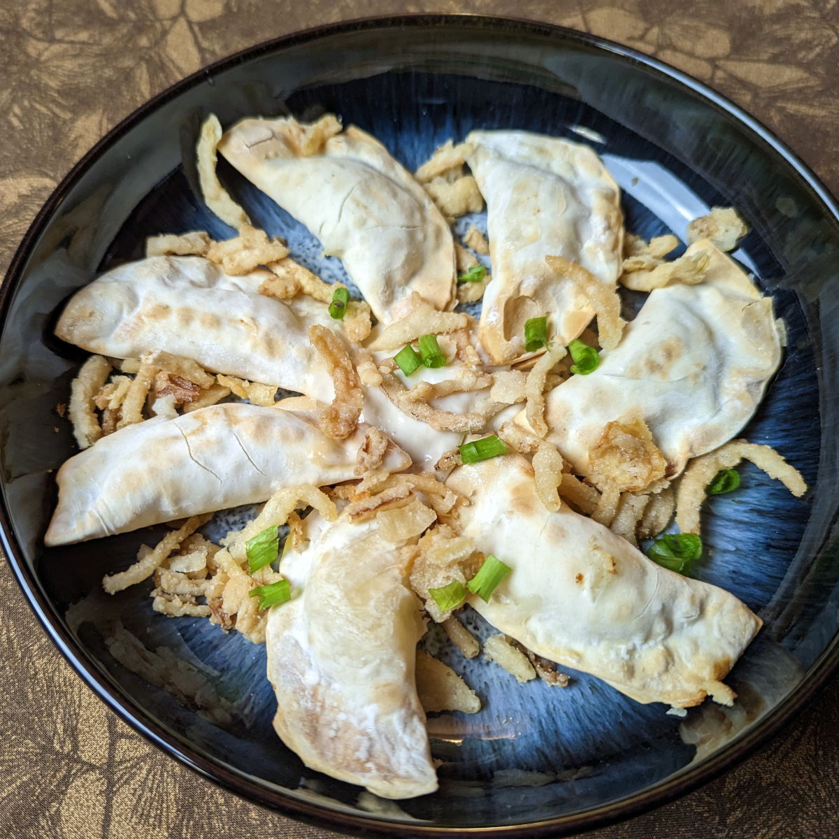 Mashed potato air fryer perogies garnished with green onion and crispy fried onions.