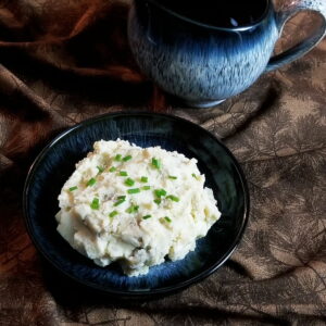 Mashed sour cream and chive potatoes in a bowl with a gravy boat in the background.