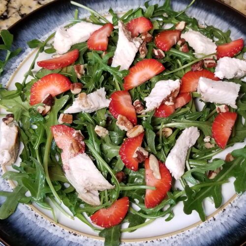 A close up of strawberry, chicken, and arugula salad with a balsamic dressing drizzle.