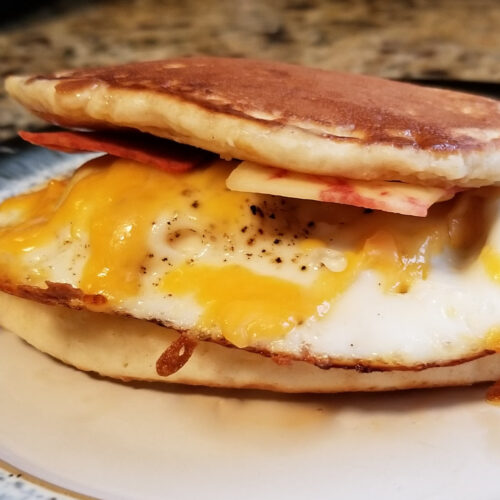 A pancake breakfast sandwich with fake bacon and an egg drizzled with syrup.