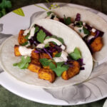 Two sweet potato tacos with cilantro, cabbage, and seasoned ranch