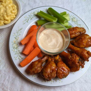Dressed air fryer chicken wings served with carrots, celery, ranch, and a side of mac and cheese.