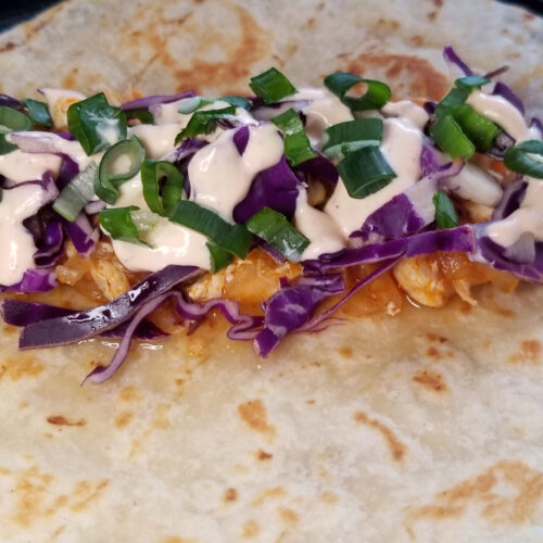 On open buffalo chicken wrap with cabbage and green onion.