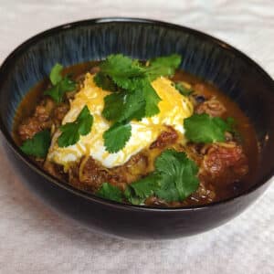 A bowl of black bean and beef chili topped with sour cream, shredded cheese, and cilantro.