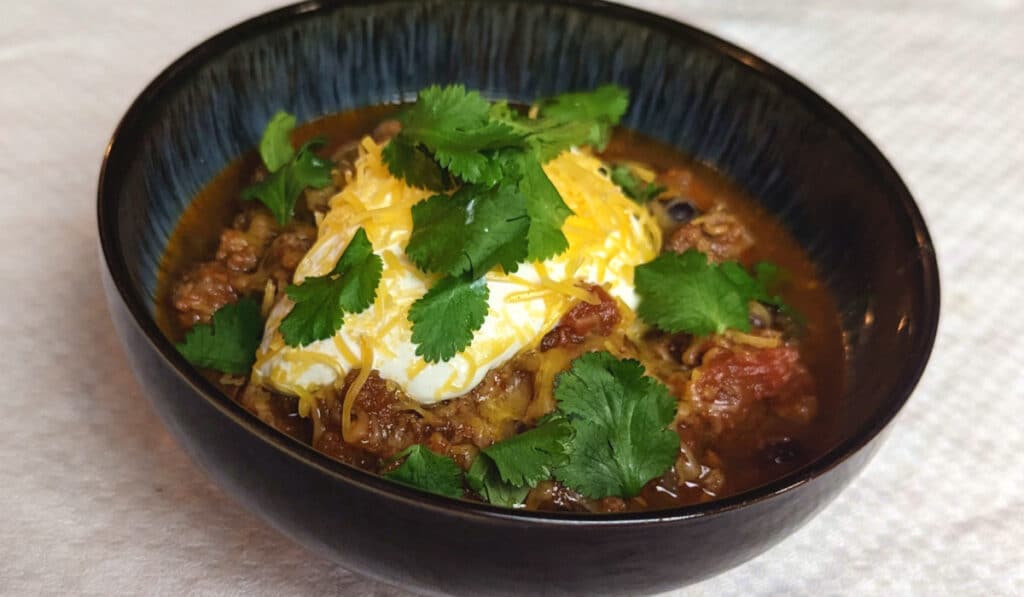 A bowl of chili with sour cream, cheddar, and herbs.